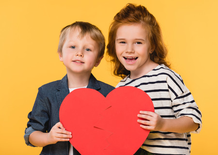 portrait of kids holding red paper heart together isolated on yellow, st valentines day conceptの写真素材