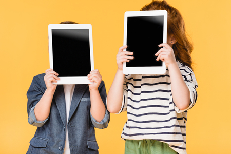 obscured view of kids holding tablets with blank screens isolated on yellowの写真素材