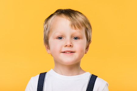 portrait of smiling little boy looking at camera isolated on yellowの写真素材