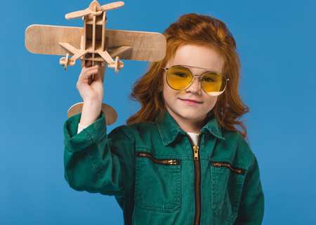 portrait of smiling child in pilot costume with wooden plane toy isolated on blue
