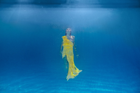underwater picture of attractive young woman in dress swimming in swimming pool