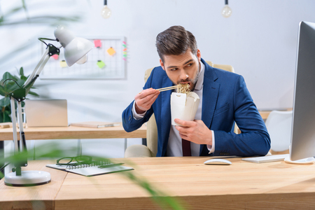 businessman eating noodles and looking at computerの写真素材