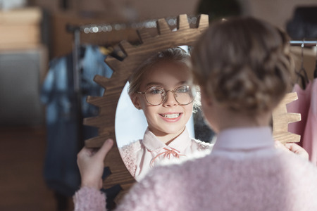 happy child in glasses looking at mirror in her hands at store interiorの写真素材