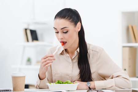 portrait of businesswoman eating take away salad for lunch in officeの写真素材