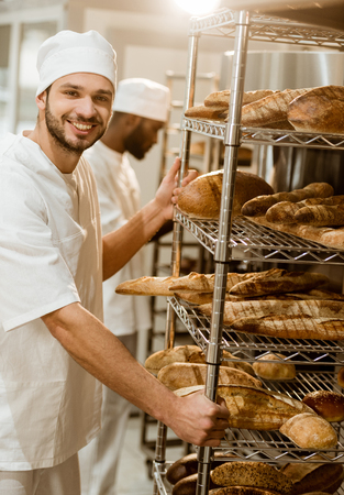 baker near shelves with fresh bread loaves at baking manufactureの写真素材