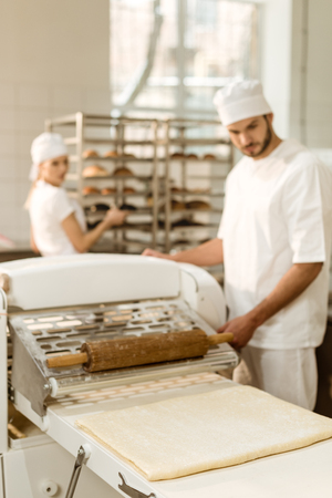 handsome young baker working with industrial dough roller at baking manufactureの写真素材