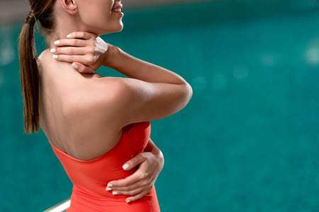 cropped shot of smiling young woman in red swimsuit posing near pool in spa center