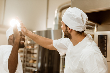 handsome young bakers giving high five at baking manufactureの写真素材