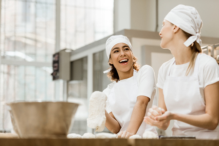 laughing female bakers kneading dough together at baking manufactureの写真素材