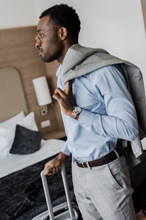 side view of african american businessman with luggage in hotel roomの写真素材