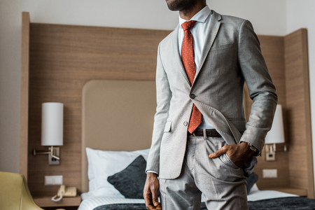 cropped view of businessman in gray suit and red tie standing in hotel roomの写真素材
