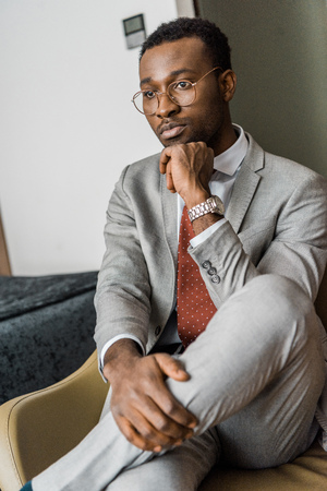 thoughtful african american businessman in gray jacket sitting in hotel roomの写真素材