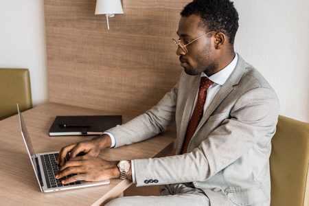 concentrated african american businessman typing on laptop in hotel roomの写真素材