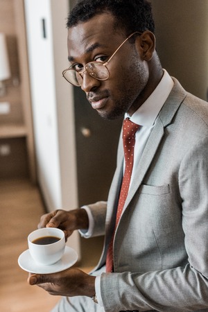 handsome african american businessman holding coffee cup in hotel roomの写真素材