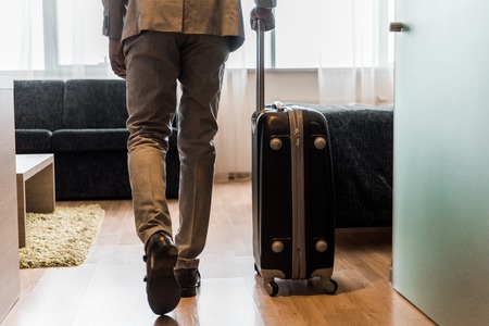cropped view of businessman in suit with baggage coming into hotel roomの写真素材
