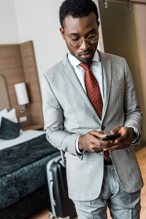 handsome african american businessman using smartphone in hotel roomの写真素材