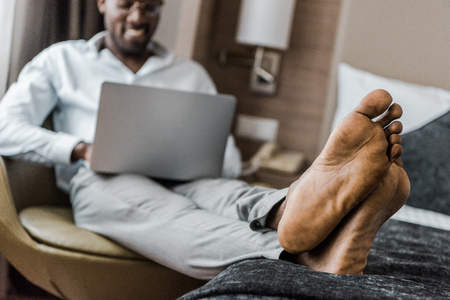 selective focus of barefoot african american man using laptop in hotel roomの写真素材