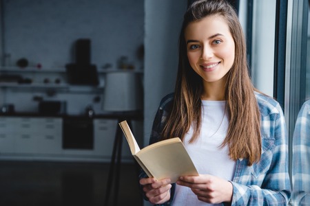 beautiful young woman holding book and smiling at cameraの写真素材
