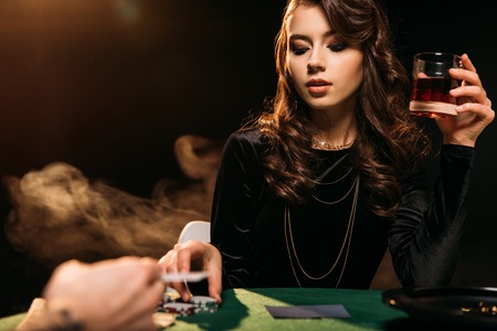 attractive girl holding glass of whiskey at poker table in casinoの写真素材