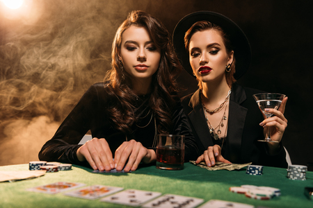 attractive girls in black clothes playing poker at table in casinoの写真素材