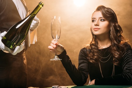 waiter pouring champagne in glass for beautiful girl at poker table in casinoの写真素材