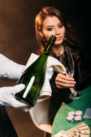 selective focus of waiter pouring champagne in glass for attractive girl at poker table in casinoの写真素材