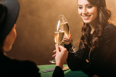 smiling attractive women clinking with glasses of champagne at poker table in casinoの写真素材
