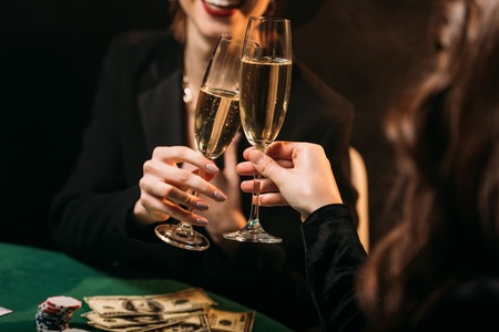 cropped image of happy girls clinking with glasses of champagne at poker table in casinoの写真素材