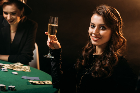 smiling attractive girl holding glass of champagne at poker table in casino and looking at cameraの写真素材