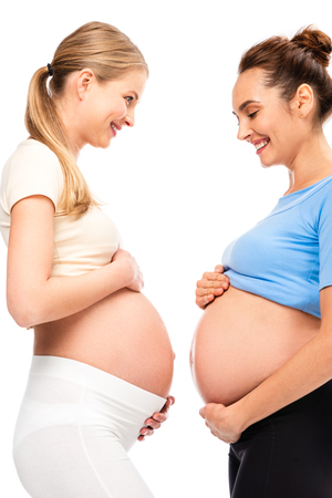 two pregnant women holding hands on bellies and smiling each other isolated on whiteの写真素材