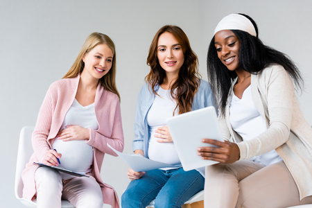 pregnant multiracial women using digital tablet at prenatal class isolated on greyの写真素材
