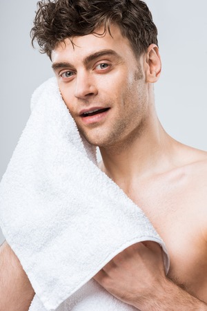 handsome young man wiping with white towel isolated on greyの写真素材