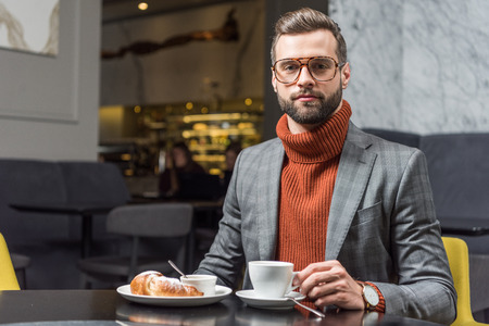 handsome man in formal wear and glasses looking at camera during lunch in restaurantの写真素材
