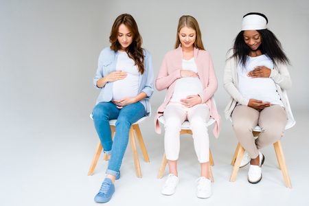 multiracial pregnant women looking down and touching belliesの写真素材