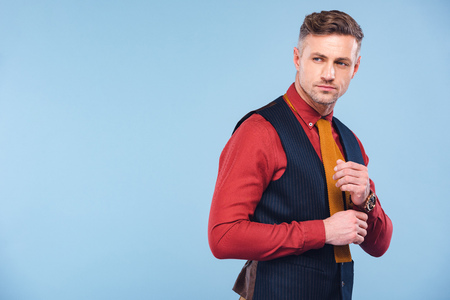 handsome stylish man in formal wear adjusting shirt isolated on blue with copy spaceの写真素材