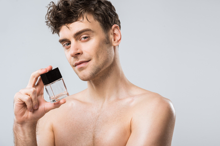 handsome smiling man holding bottle of perfumes, isolated on greyの写真素材
