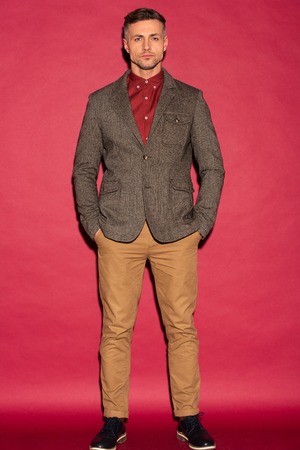 focused stylish man in formal wear looking at camera on red background