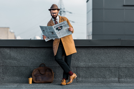 adult bearded man standing with crossed legs and reading business newspaper on roofの写真素材