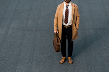 cropped view of bearded businessman standing with leather brown bagの写真素材