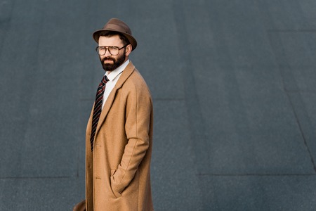 side view of bearded businessman standing in coat with hand in pocketの写真素材