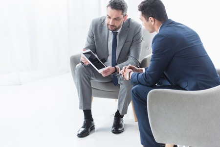 serious businessman showing digital tablet with blank screen to young colleague in officeの写真素材