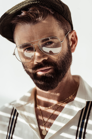 close up view of handsome bearded man in glasses and cap looking at camera on white backgroundの写真素材