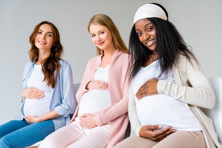 pregnant multiethnic women touching bellies during antenatal class isolated on greyの写真素材