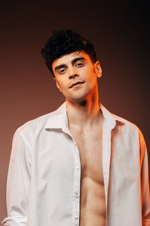 fashionable sexy man posing in white shirt, isolated on brownの写真素材