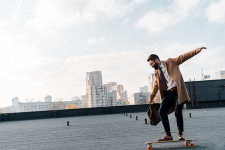 side view of businessman in coat and formalwear riding on penny boardの写真素材