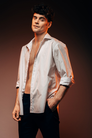 sexy stylish man posing in white shirt, isolated on brownの写真素材