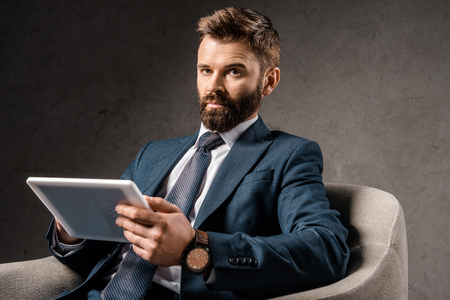 confident businessman holding digital tablet and sitting in armchairの写真素材
