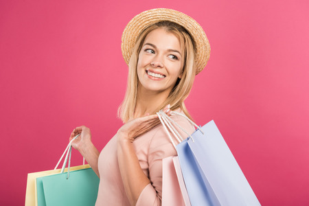 attractive smiling woman in straw hat holding shopping bags, isolated on pinkの写真素材