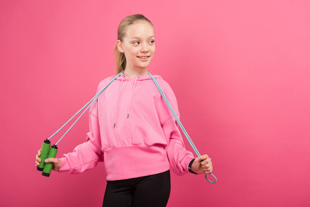 adorable child in sportswear posing with skipping rope, isolated on pinkの写真素材