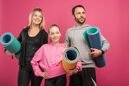 sporty family with daughter holding fitness mats, isolated on pinkの写真素材